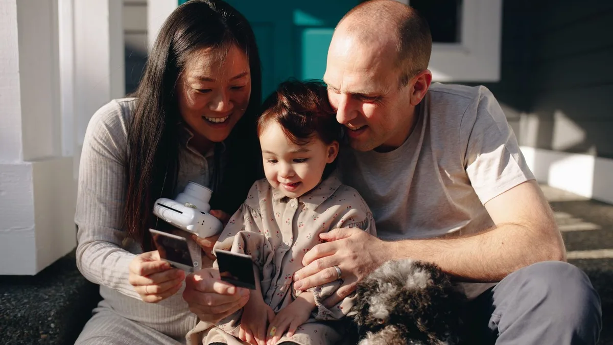 A young military family with their toddler and dog sitting on the front steps of their home in the afternoon sun
