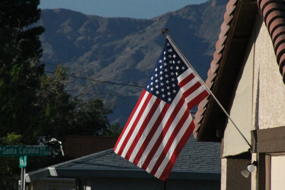 An American flag mounted on the eaves of a stucco home with a barrel tile roof in North Las Vegas, Nevada, with single story houses and the desert mountains behind it