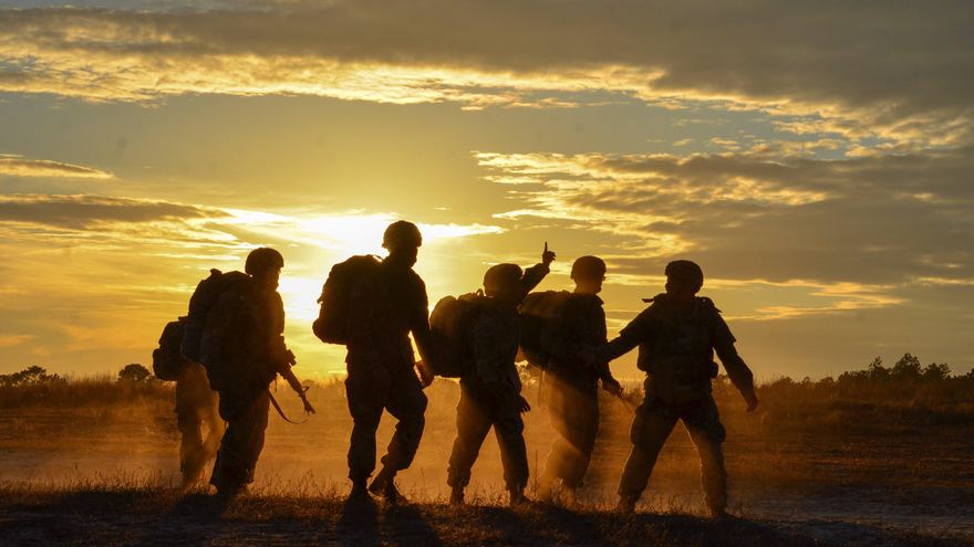 Service members walking across an open field at sunset, silhouetted against a gold sky